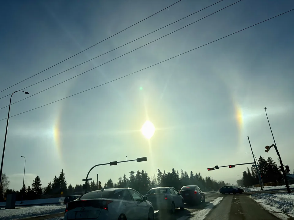 Bright spots on either side of the sun above a road intersection.