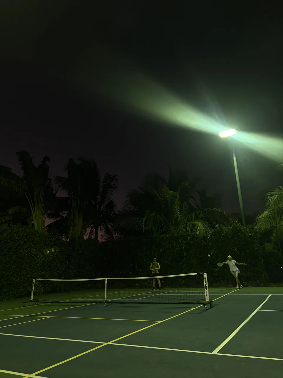 Tennis players under a bright floodlight at night.