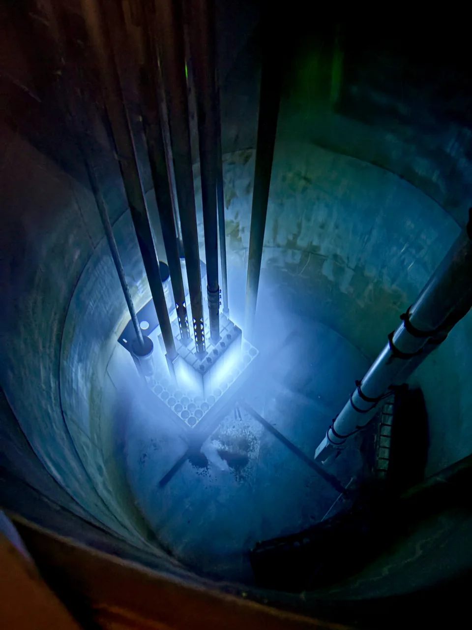 Blue light beneath the water of a reactor pool, viewed from above.